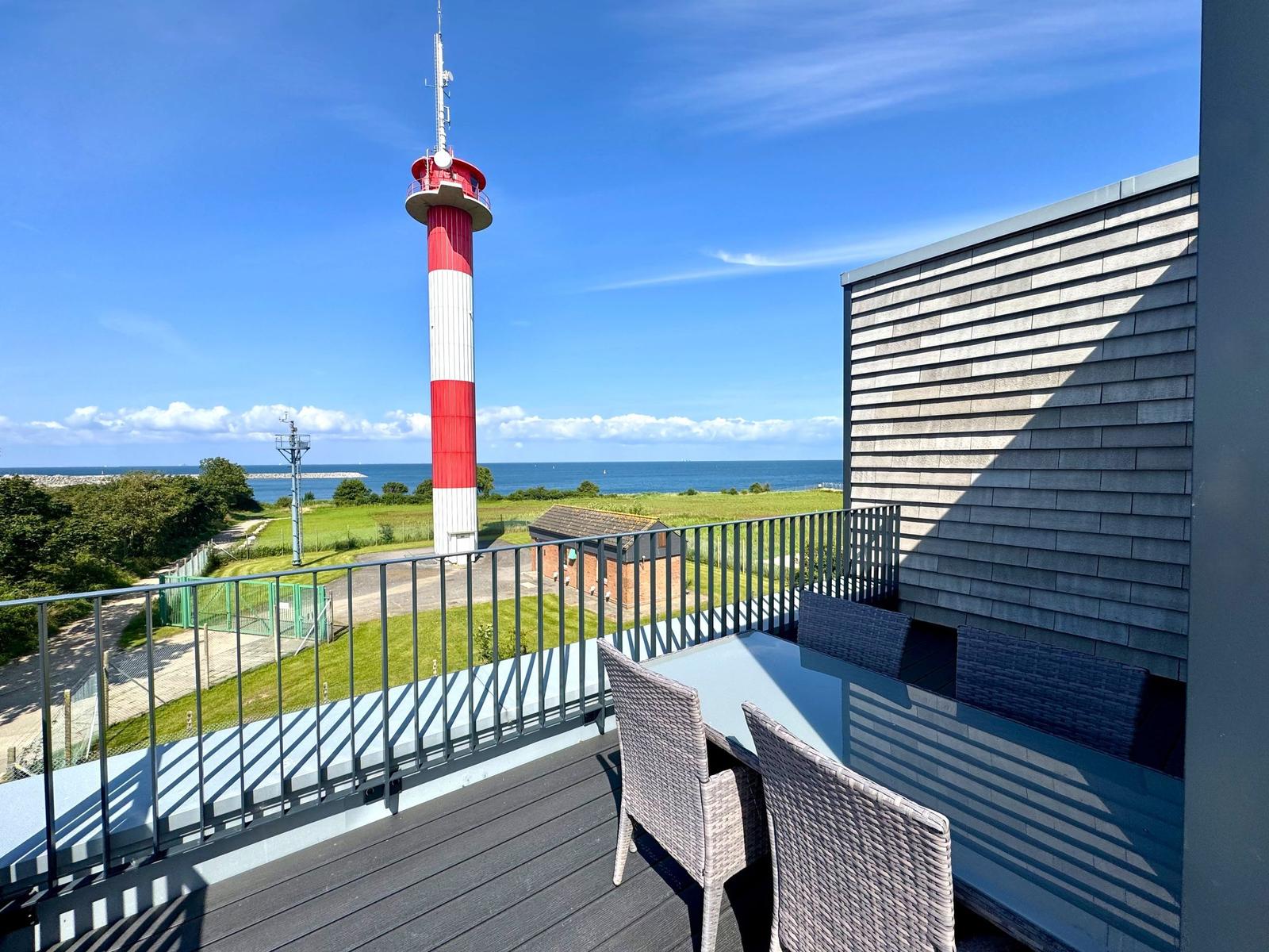 Terrasse mit Tisch und Stühlen, Blick auf Leuchtturm und Meer.