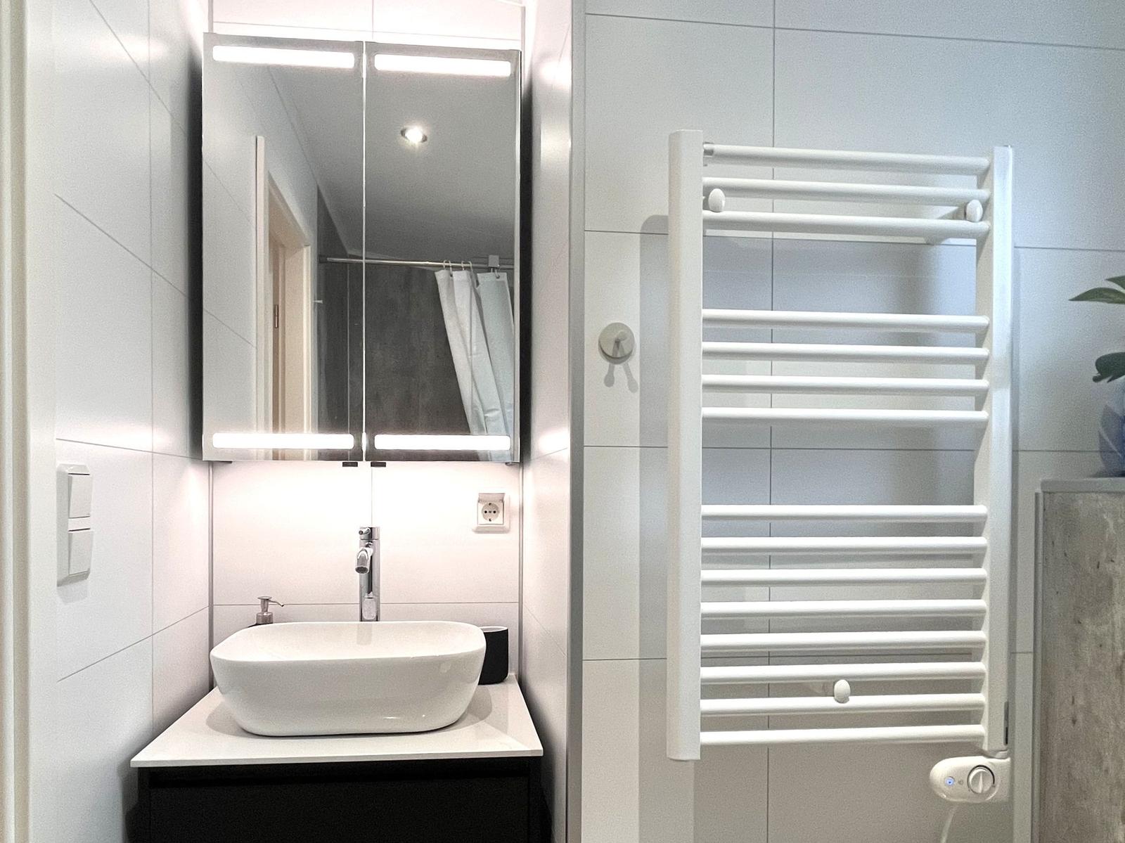 Badezimmer mit Waschbecken, Spiegel und Handtuchheizung.
