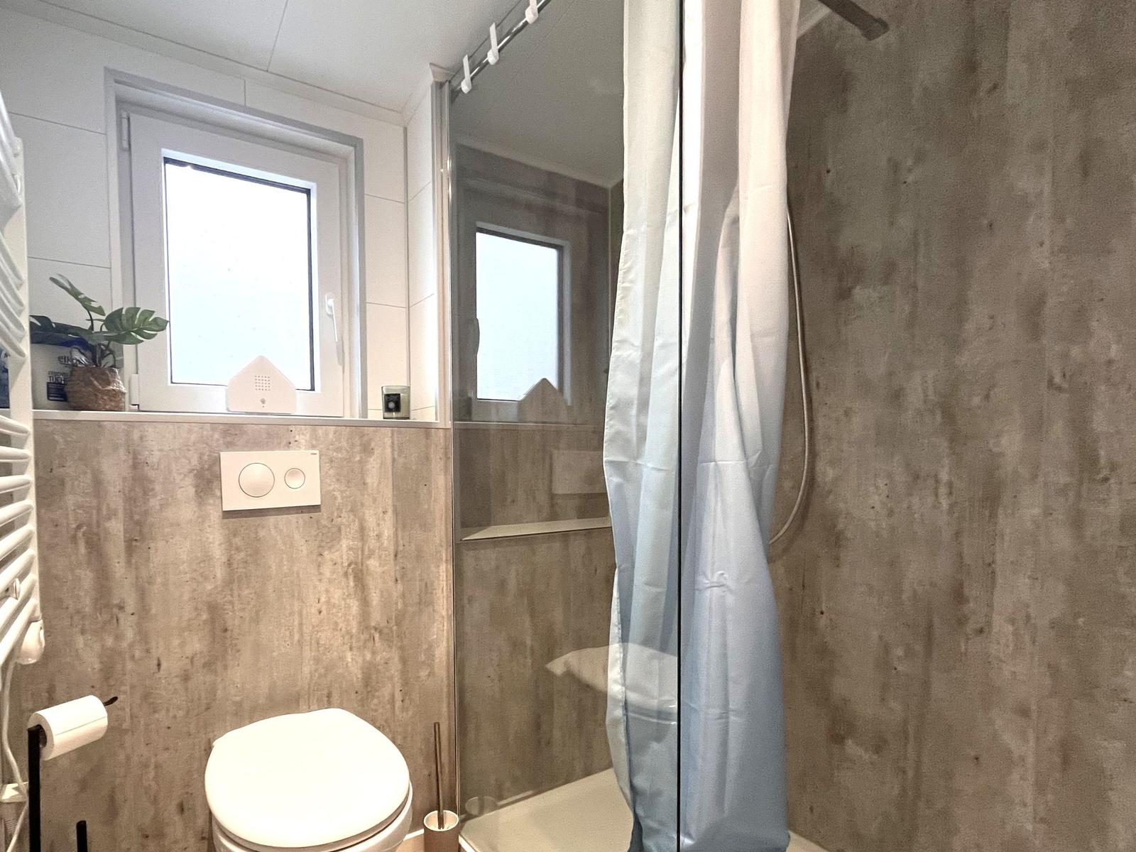 Badezimmer mit Dusche, Toilette und Fenster.