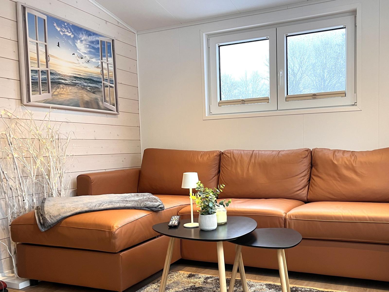 Ein Wohnzimmer mit braunem Sofa, Tisch und Fenstern.