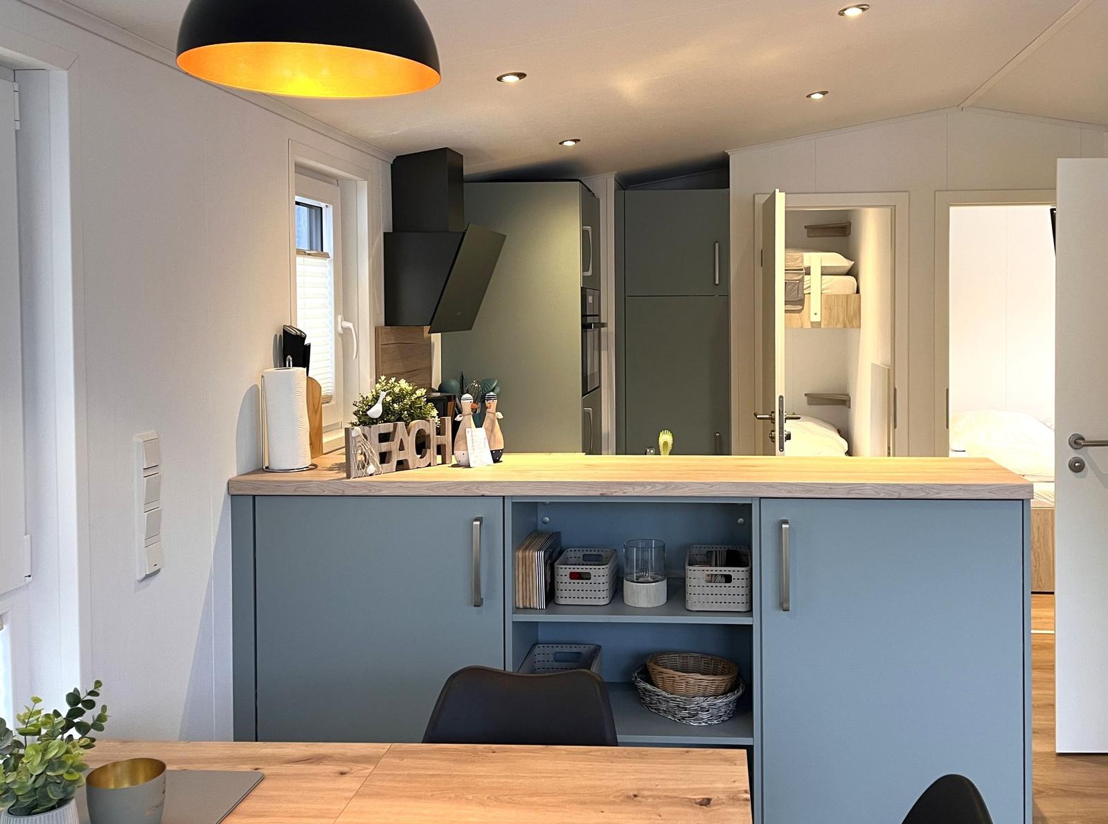 Küche mit blauen Schränken und Holzoberfläche. Im Hintergrund sind Schlafzimmer sichtbar.