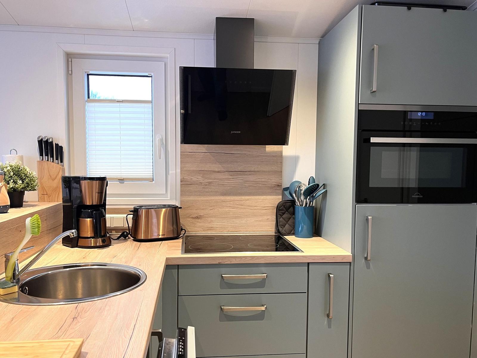 Küche mit Dunstabzug, Herd und Kühlschrank. Holzoberflächen und graue Schränke.