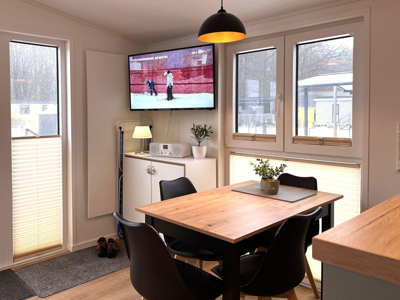 Essbereich mit Tisch, Stühlen und Fernseher an der Wand.