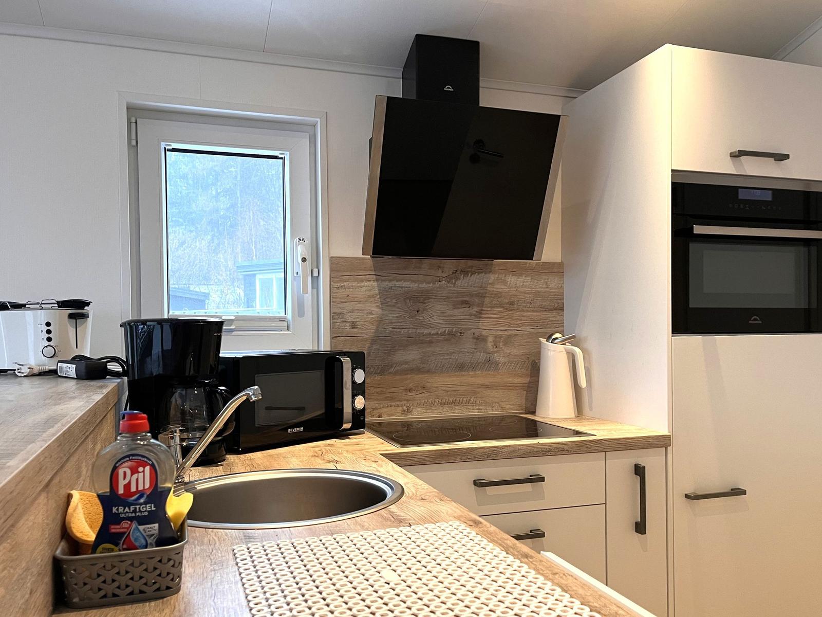 Küche mit Spüle, Dunstabzug, Kühlschrank und Fenster.