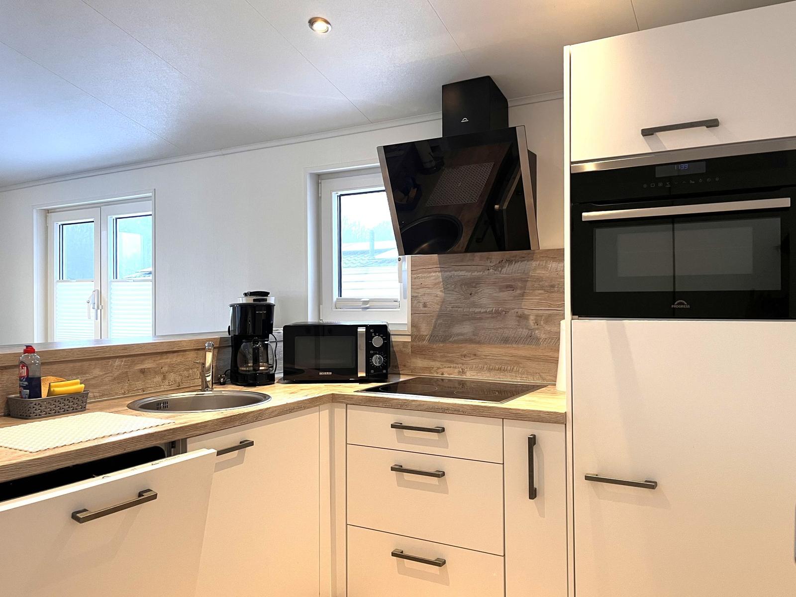 Küche mit Spüle, Herd, Mikrowelle und Backofen. Holzoberflächen und weiße Schränke.