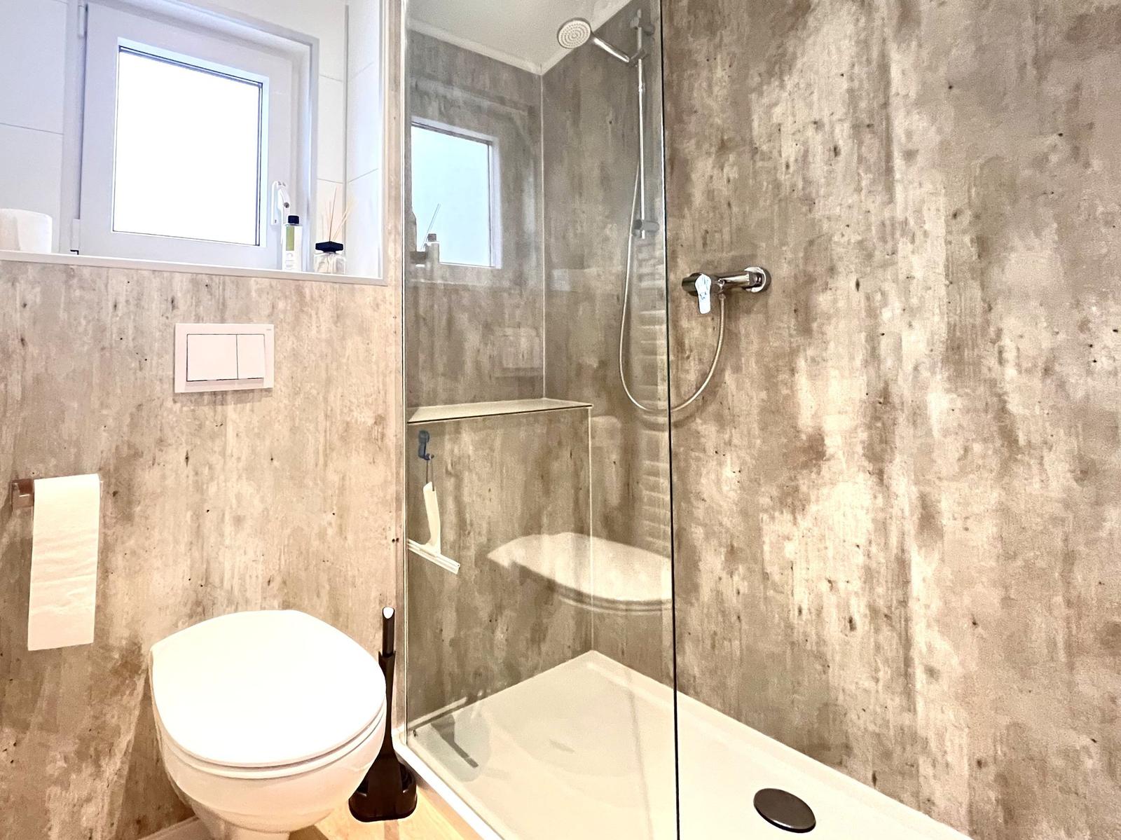 Badezimmer mit Dusche, Toilette und Fenster