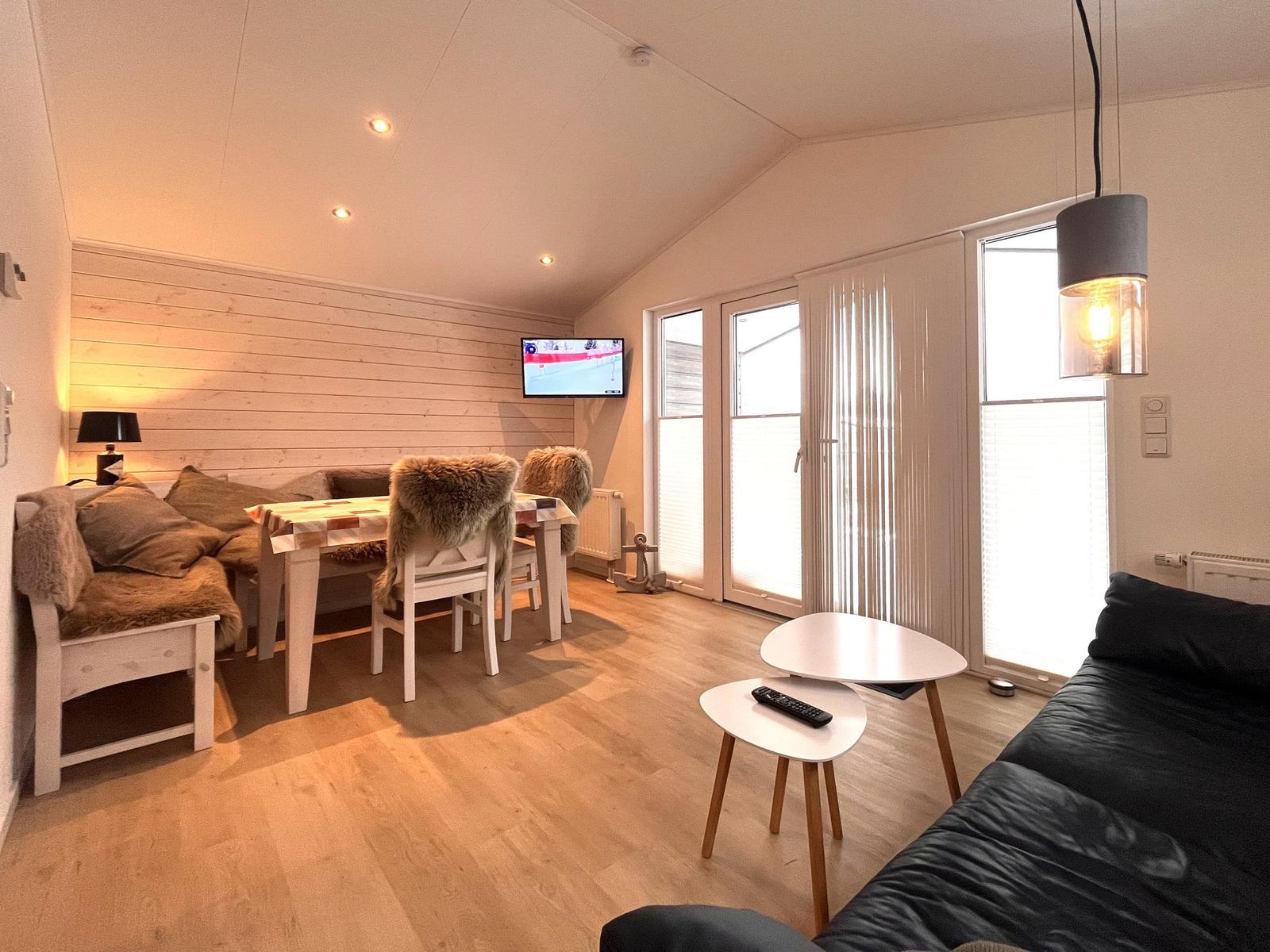 Wohnbereich mit Sofa, Esstisch, TV und Fenster zur Außentür.