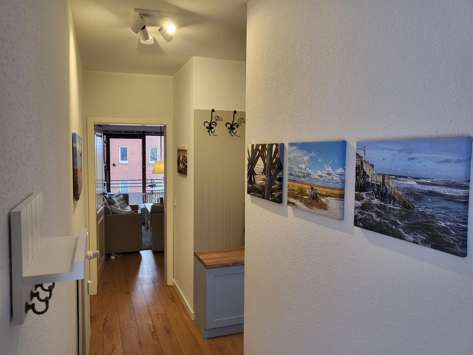 Flur mit Wandbildern und Blick in Wohnbereich mit Sofa und Balkon.