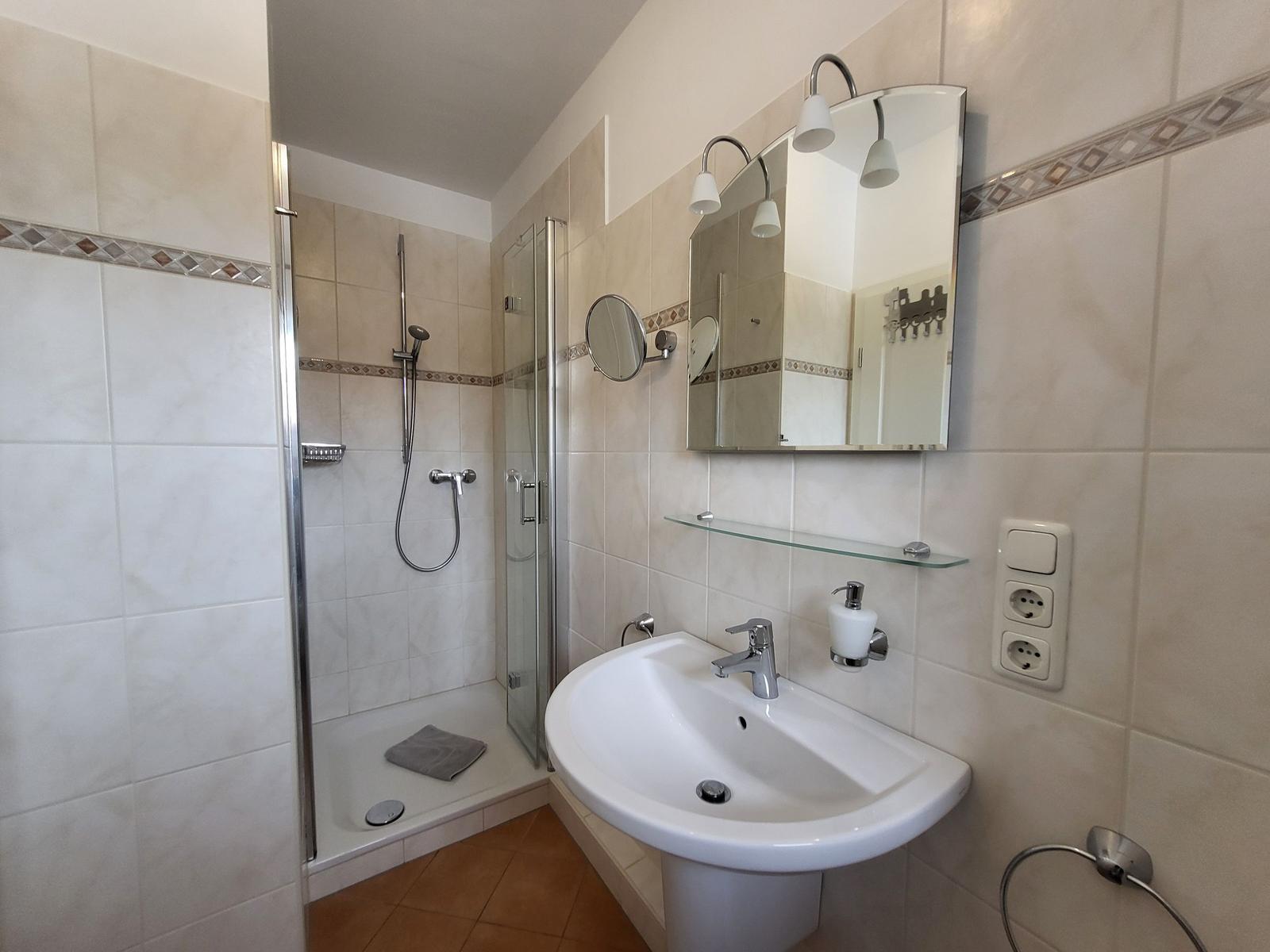 Badezimmer mit Dusche, Waschbecken und Spiegel