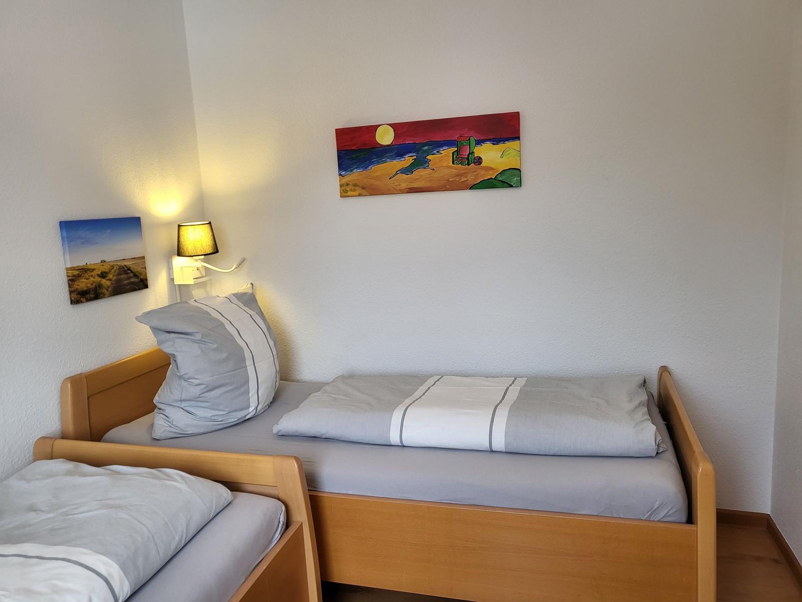 Zwei Betten mit grauer Bettwäsche, Wandbilder und eine Stehlampe.