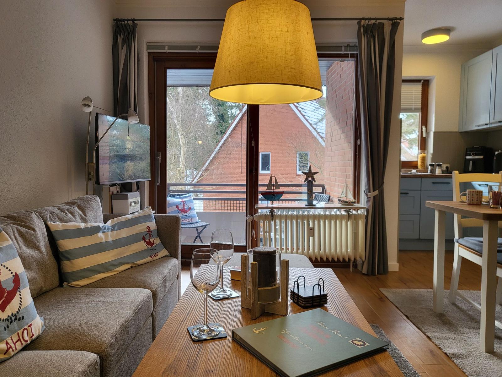 Wohnzimmer mit Sofa, Couchtisch und Balkonansicht. Küche im Hintergrund.