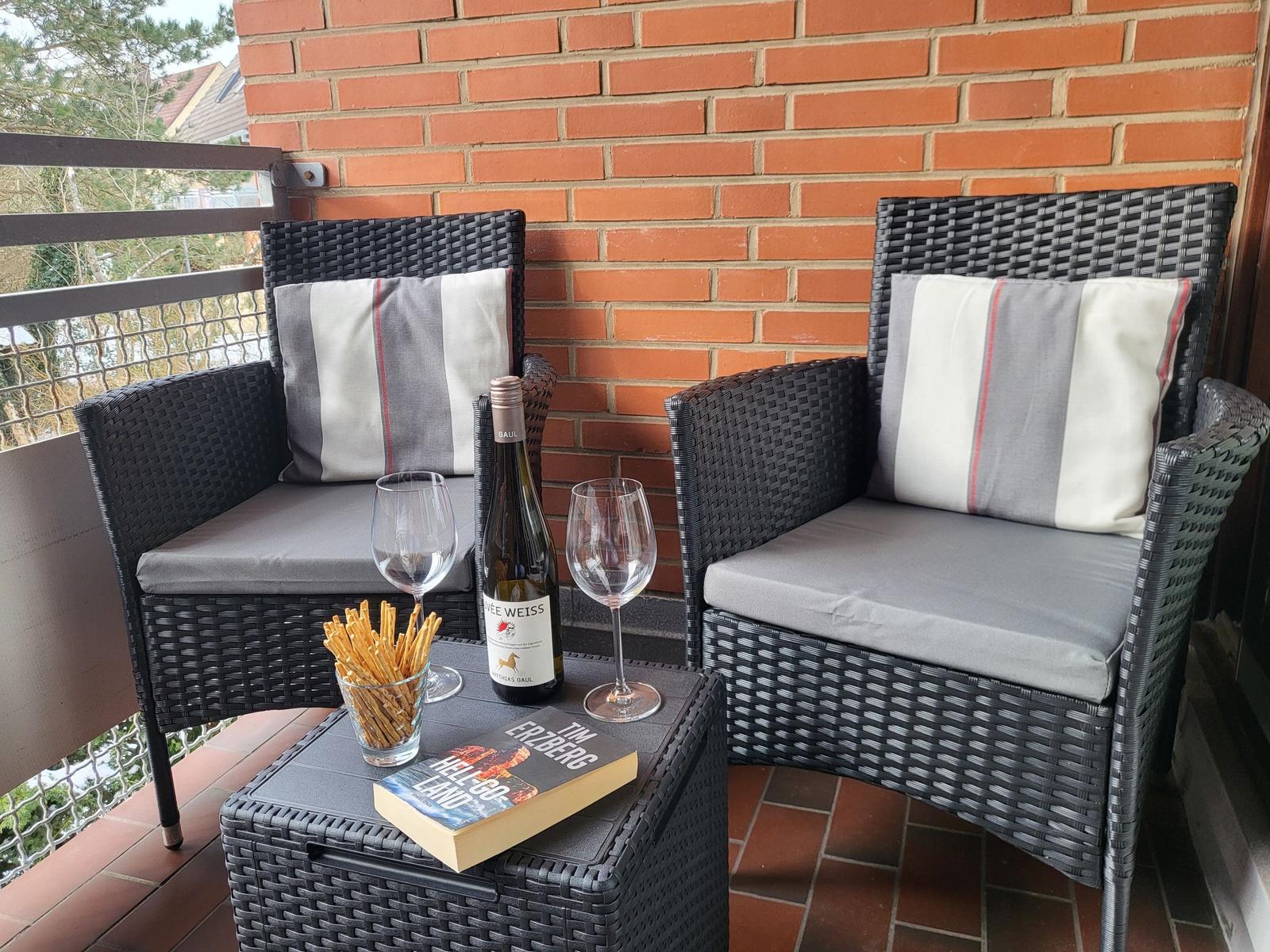 Zwei Sessel mit Kissen und Tisch mit Wein, Gläsern und Buch auf Balkon.
