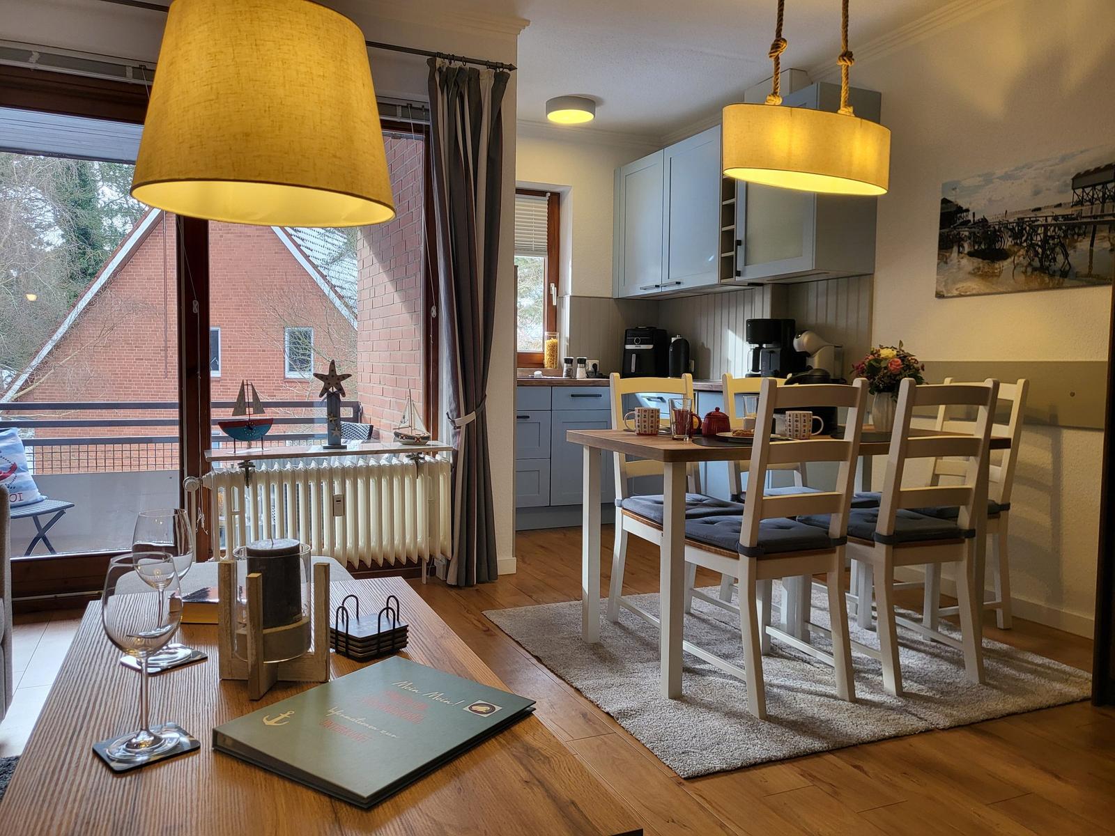 Esszimmer mit Tisch, Stühlen und Küchenbereich. Balkon mit Blick auf Haus.