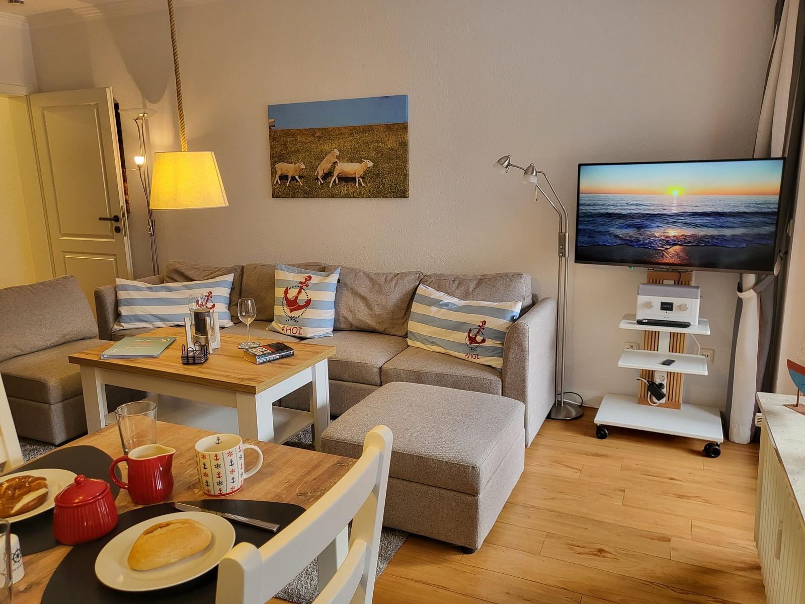 Wohnzimmer mit Sofa, Fernseher und Esstisch mit Speisen.