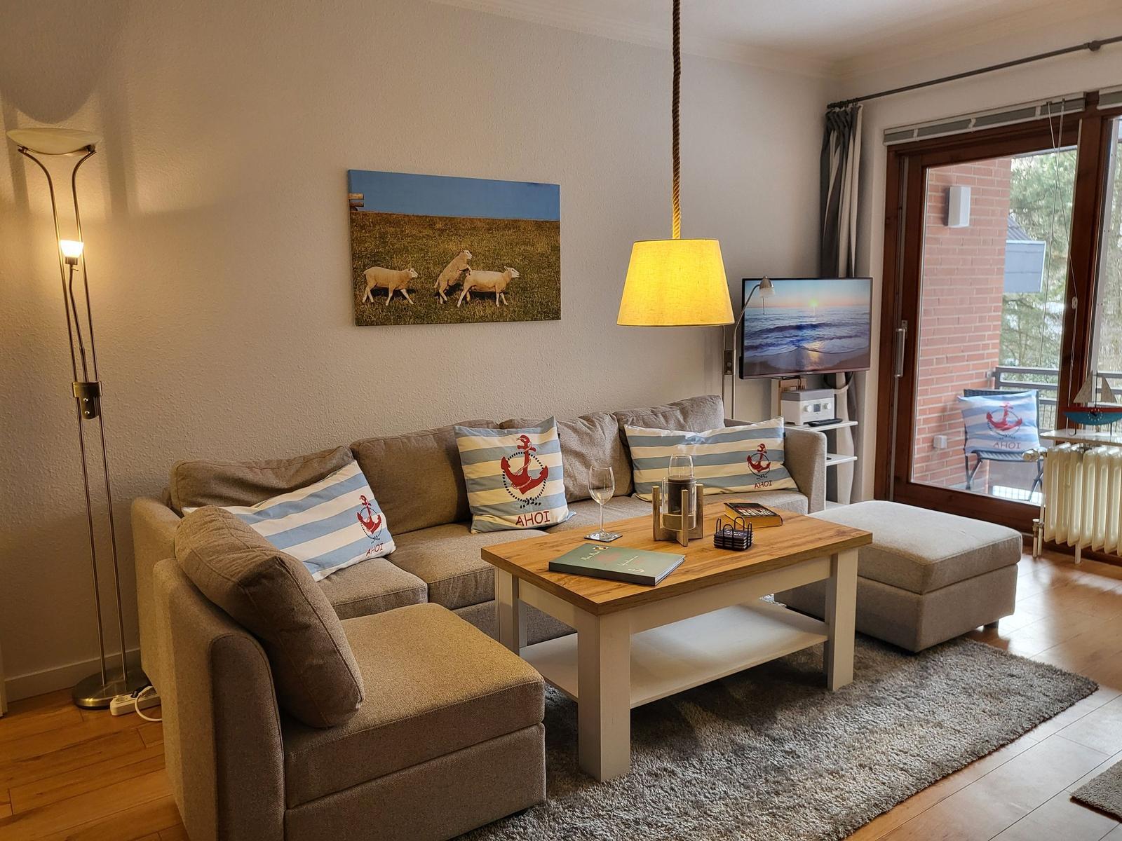 Wohnzimmer mit Sofa, Couchtisch und Fernseher. Durchgang zur Terrasse.