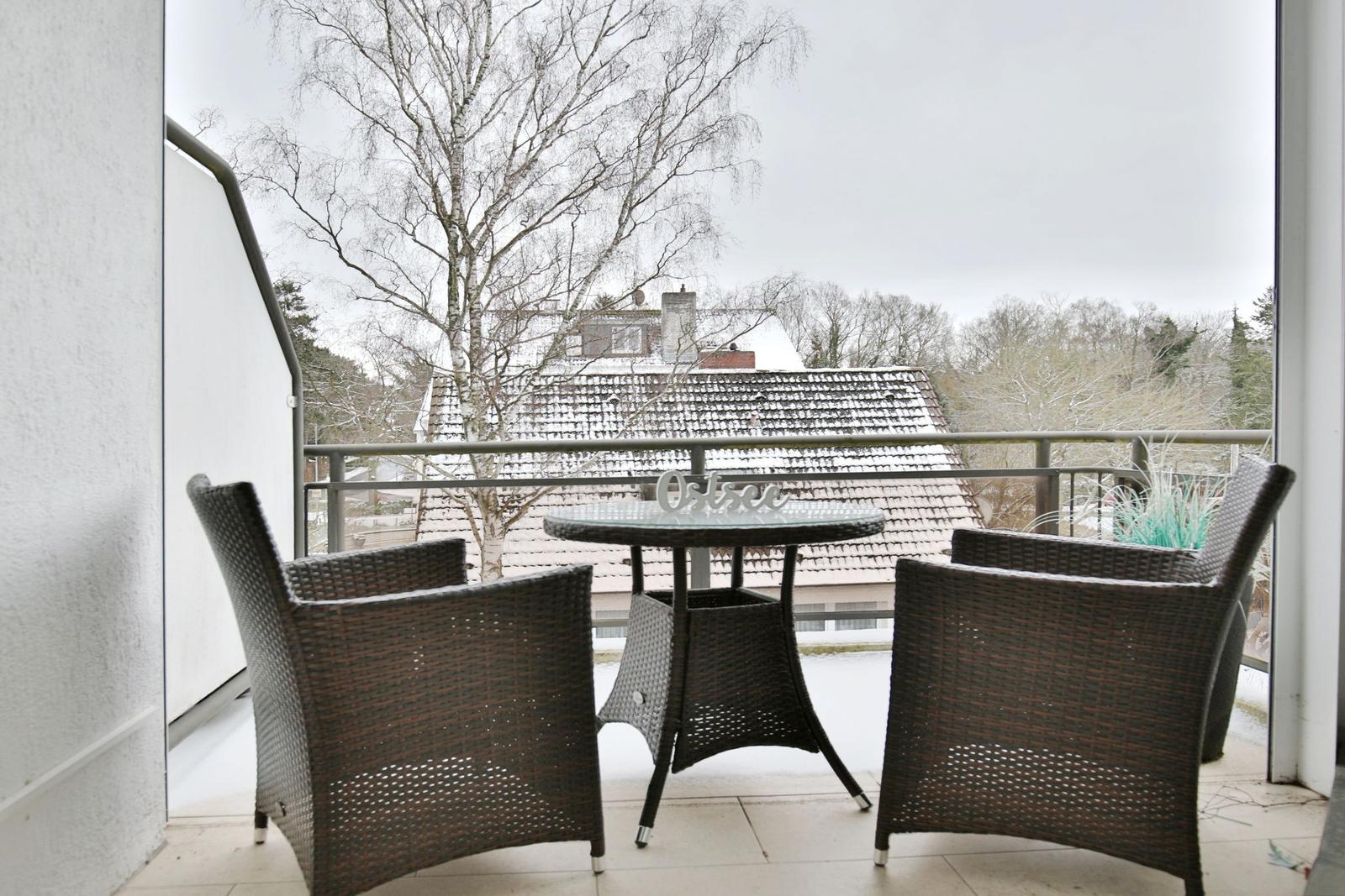 Terrasse mit Tisch und Stühlen, Blick auf schneebedeckte Dächer und Bäume.