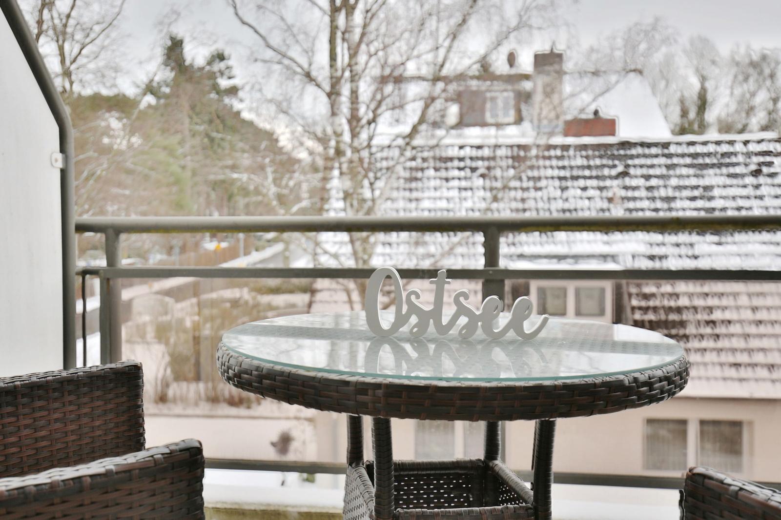 Terrasse mit Tisch und Stühlen, Blick auf schneebedeckte Dächer und Bäume.