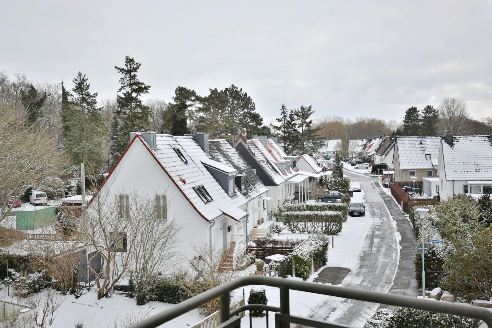Schneebedeckte Häuserzeile mit Straße und Bäumen im Winter