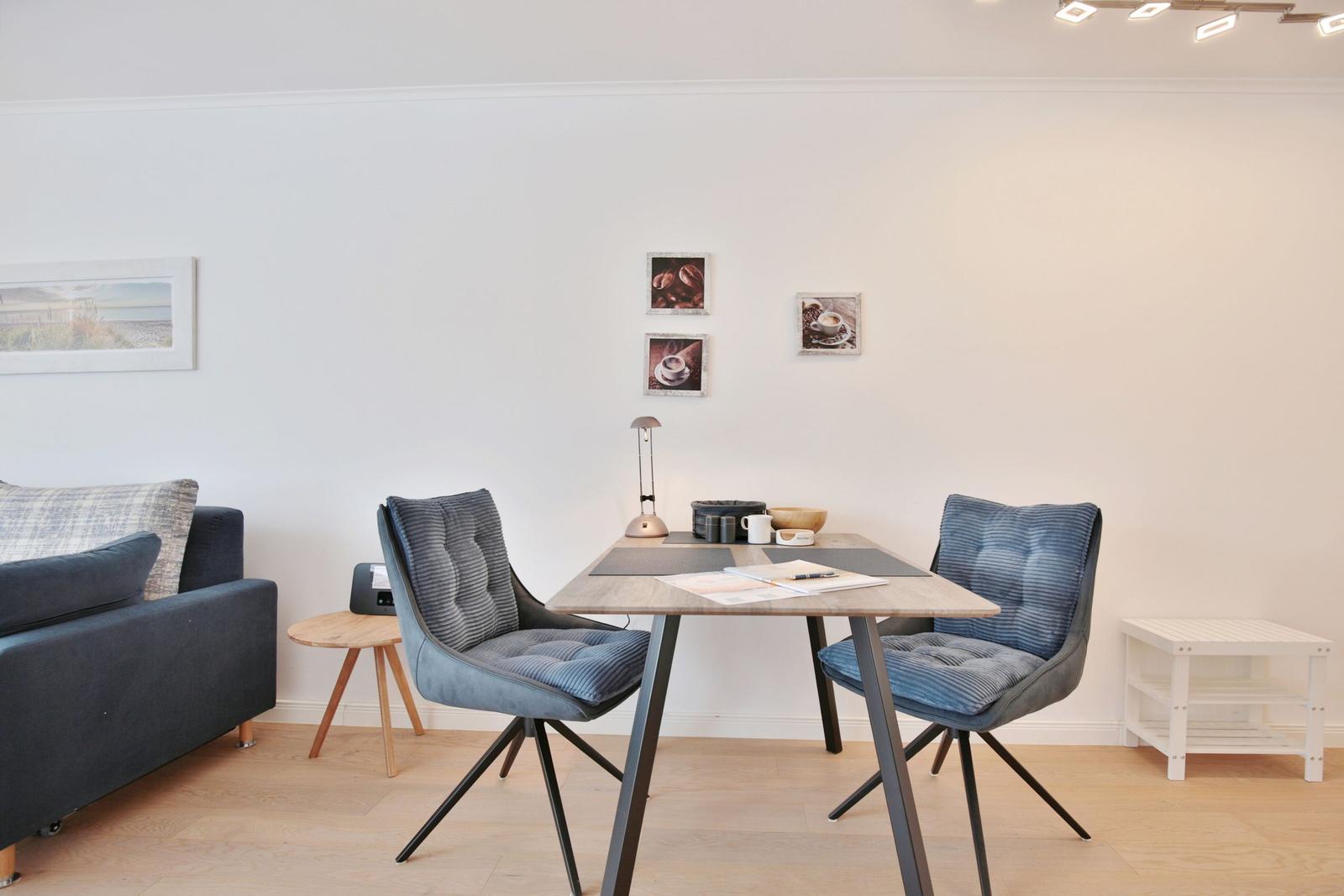 Essbereich mit Tisch und zwei Stühlen, Sofa und Wandbilder