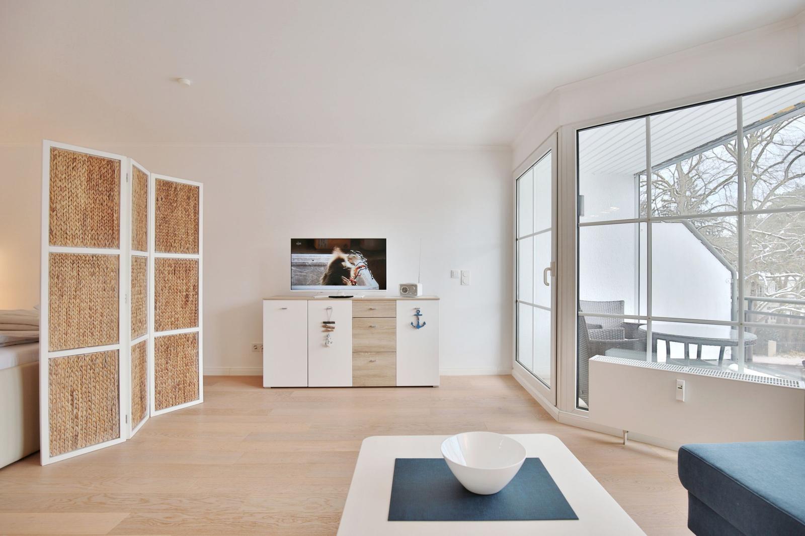 Wohnzimmer mit Fernseher, Schiebetür und Sicht auf Balkon