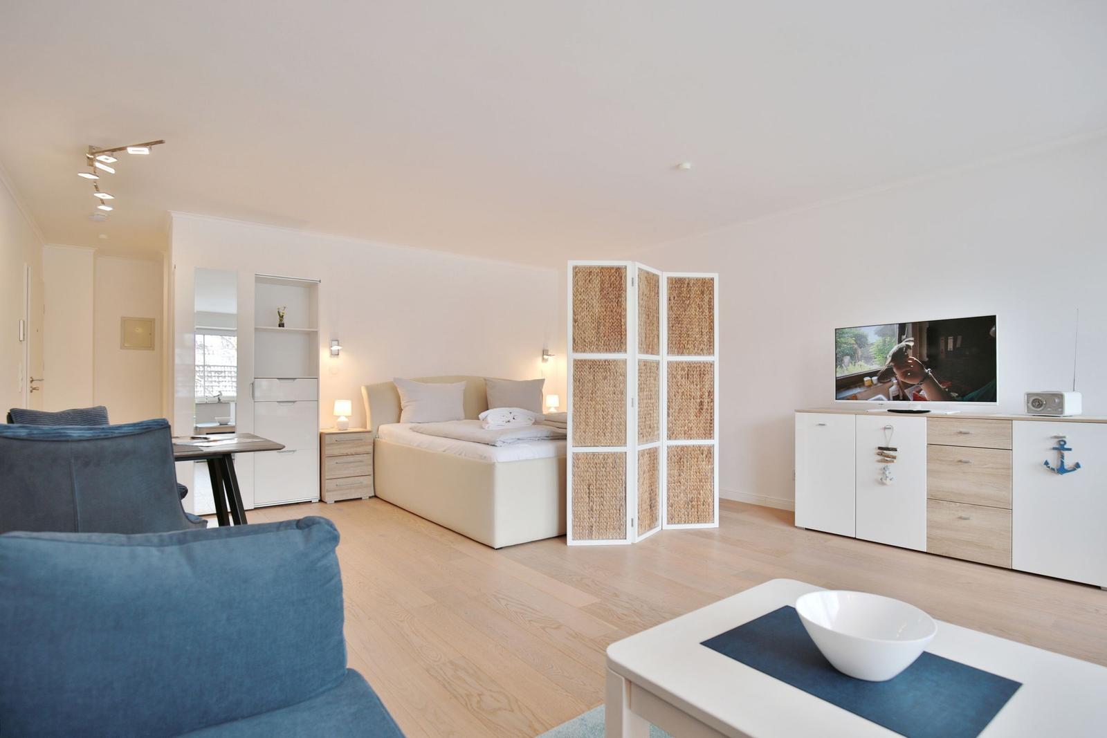 Ein Raum mit Bett, TV und Sitzgelegenheiten auf hellem Holzboden.