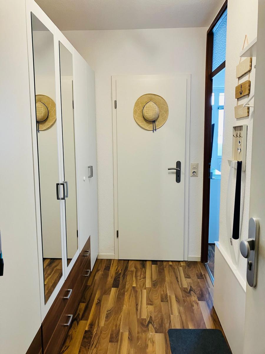 Flur mit Spiegelschrank, Holzboden und Tür mit Strohhut