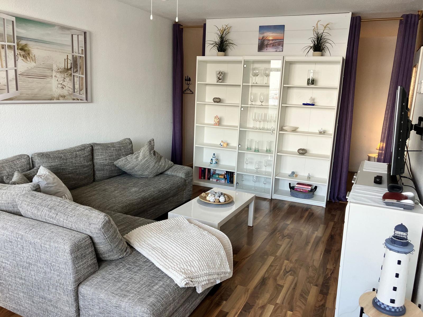 Wohnzimmer mit grauem Sofa, weißen Regalen und Holzboden.