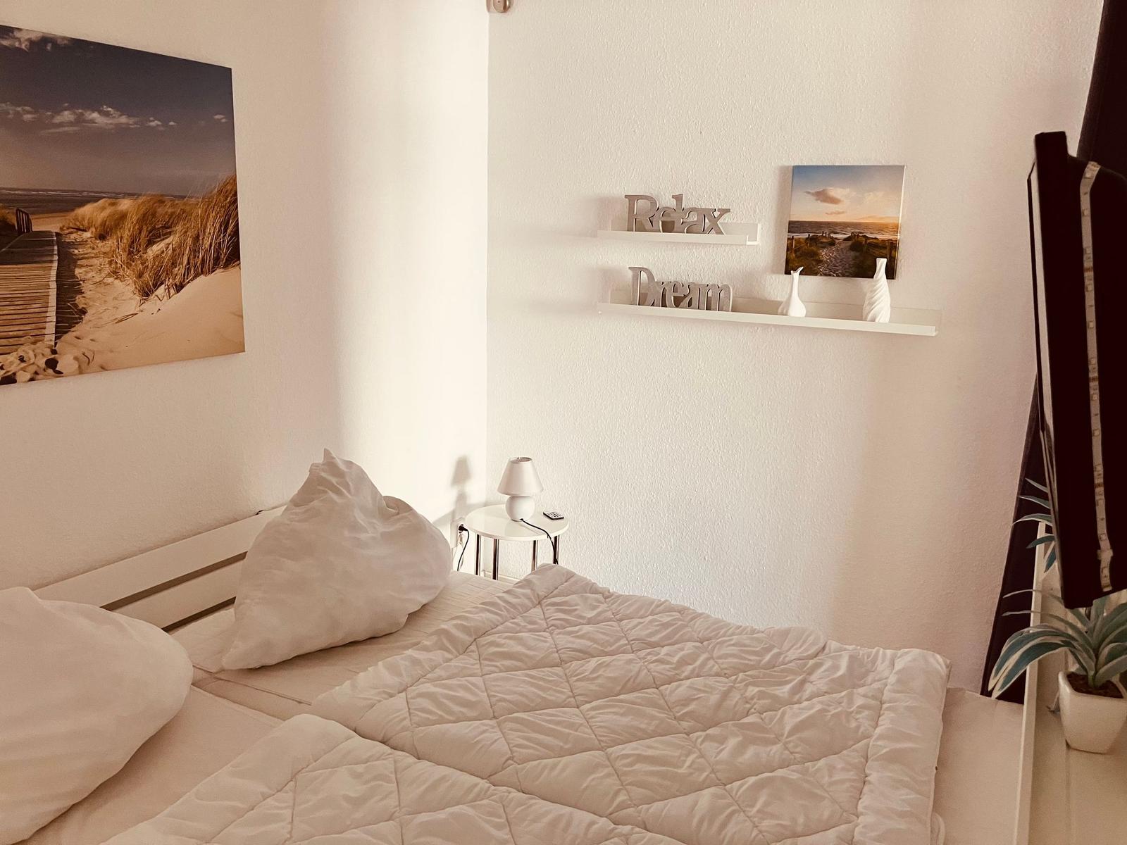 Schlafzimmer mit Bett, Wandbild und Regal mit Dekoration.
