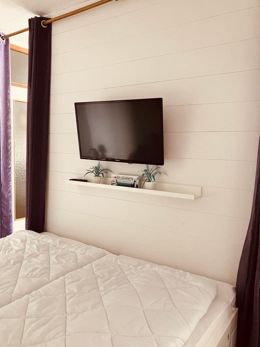 Schlafzimmer mit Bett, Wand-TV und Pflanzen auf Regal