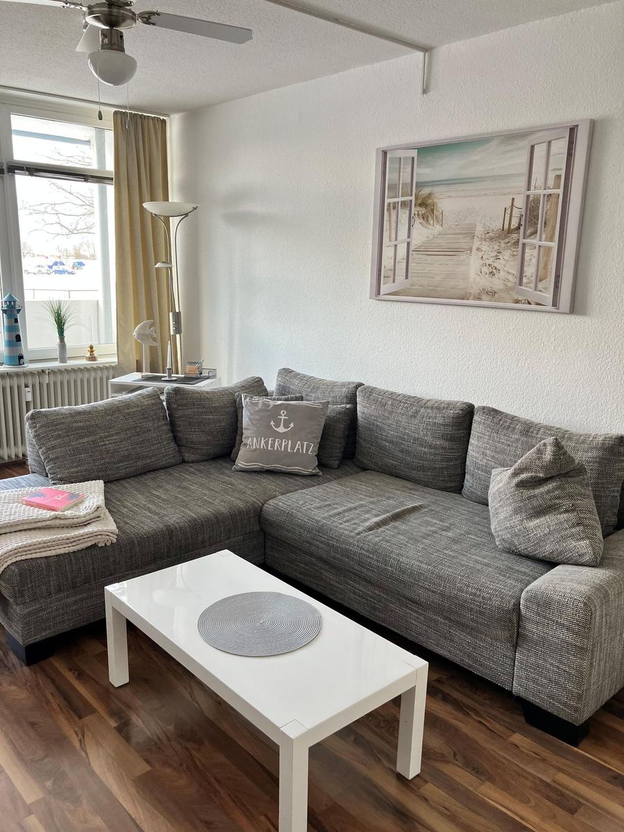 Wohnzimmer mit grauem Ecksofa, weißem Tisch und Wandbild