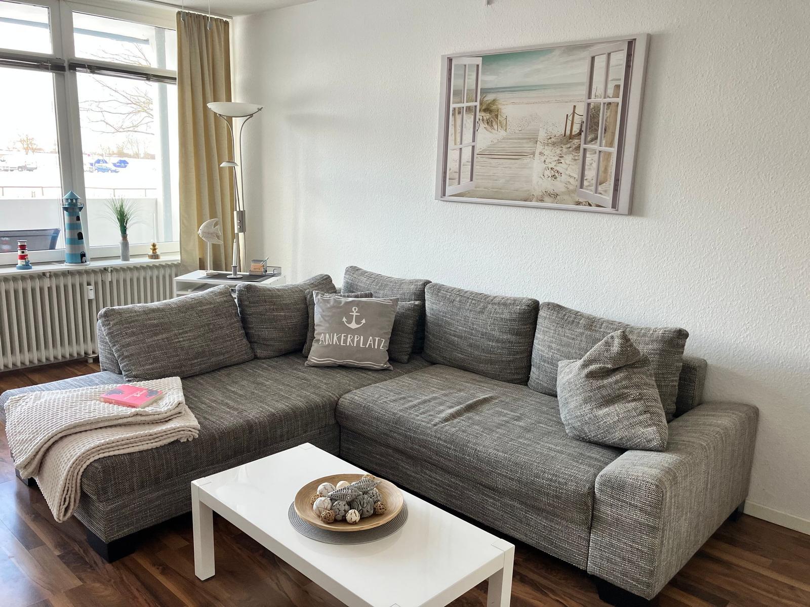 Ein Wohnzimmer mit grauem Sofa, weißem Tisch und Wandbild.