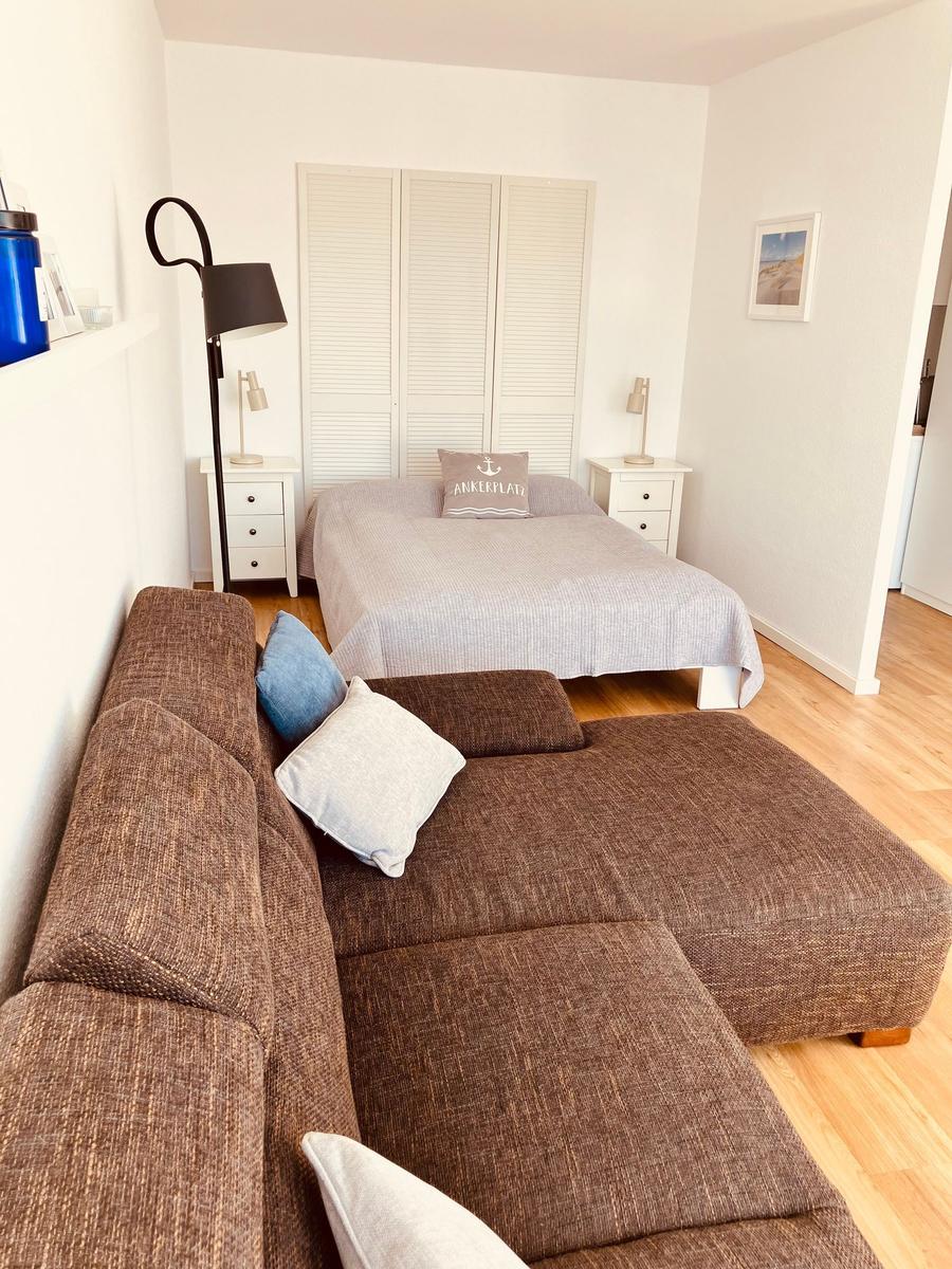 Schlafzimmer mit Bett, Schrank und Sofa. Holzboden und weiße Wände.