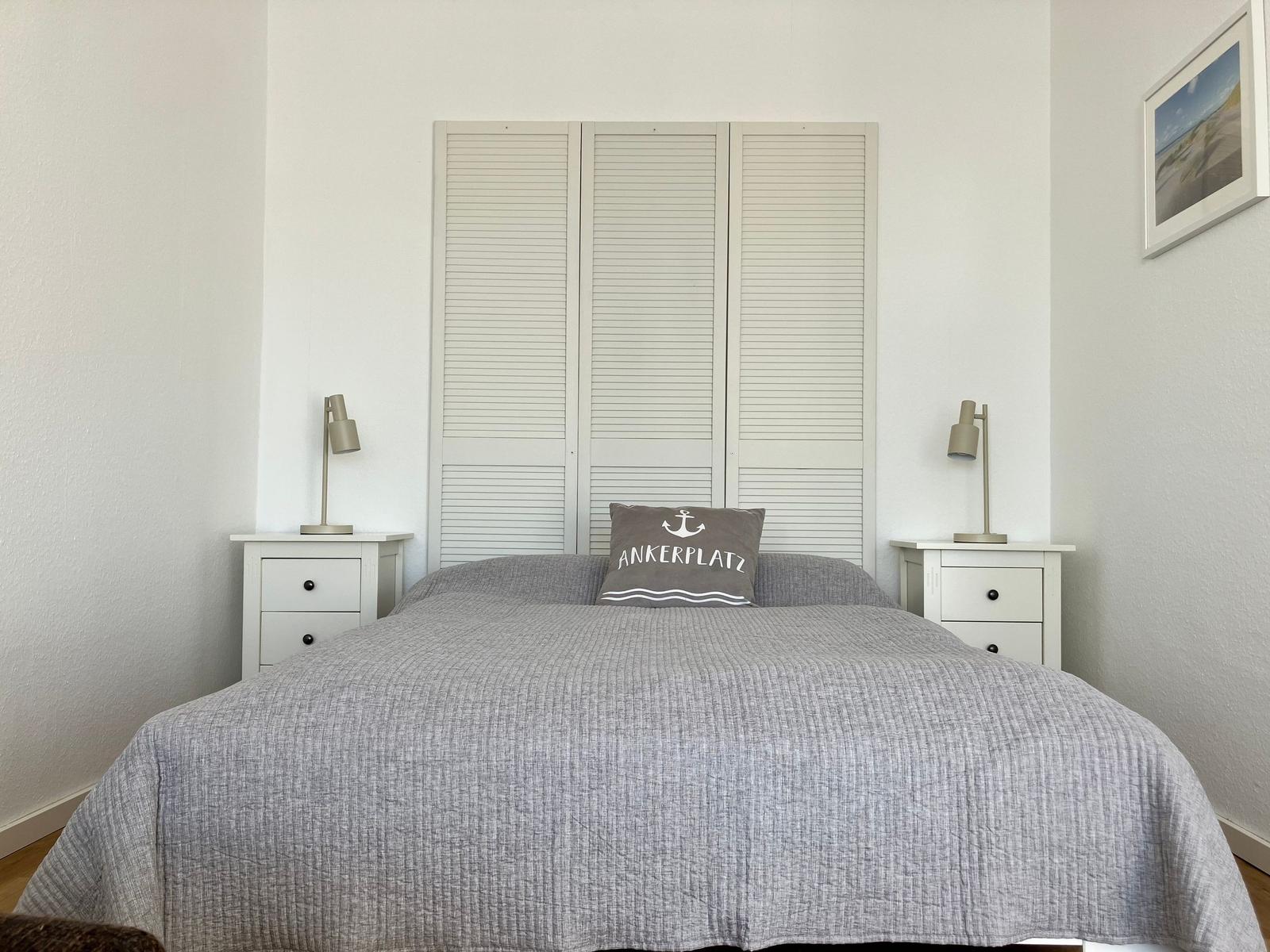 Schlafzimmer mit Bett, Nachttischen und Schrank. Kissen mit Ankerplatz Aufdruck.
