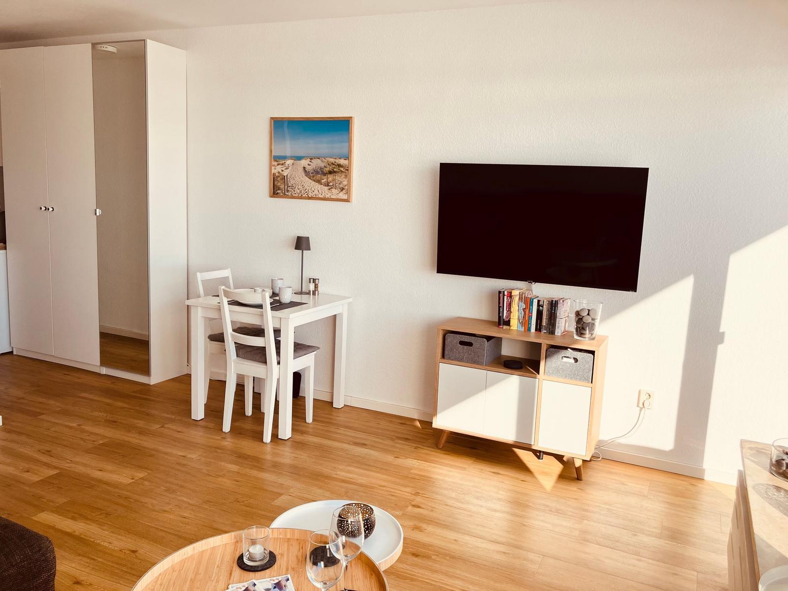 Wohnzimmer mit Esstisch, Fernseher und Kleiderschrank.
