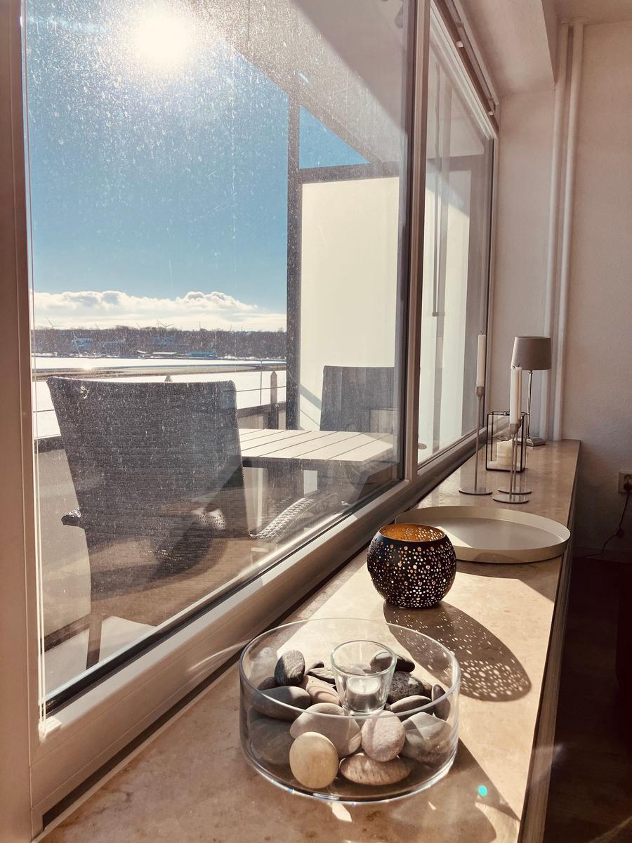Großes Fenster mit Blick auf Hafen und Terrasse mit Stuhl und Tisch.