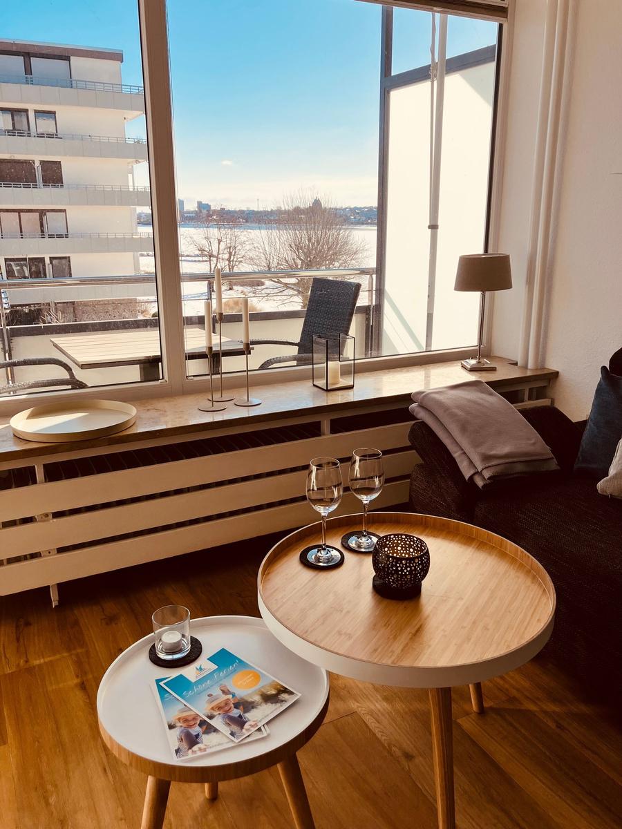 Wohnzimmer mit Blick auf Fluss und Balkon. Holztische, Gläser und Dekoration.