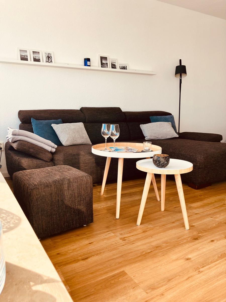 Ein Wohnzimmer mit braunem Sofa, zwei runden Tischen und Holzboden.