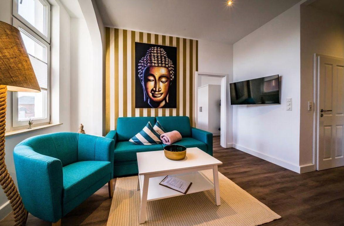 Wohnzimmer mit türkisfarbenem Sofa und Sessel, Wandbild Buddha und Flachbildschirm.