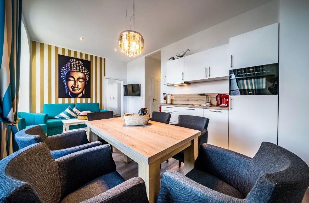 Essbereich mit Holztisch und Stühlen, Küchenzeile und Buddha-Bild an der Wand.