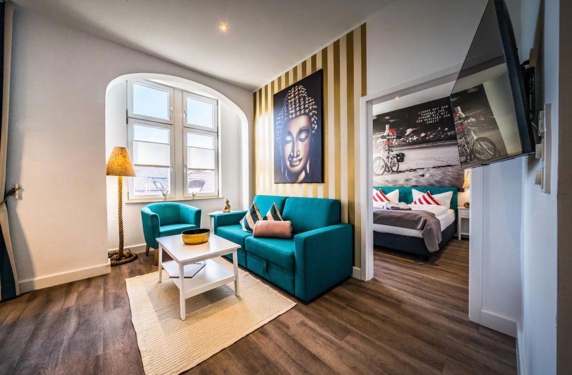 Wohnzimmer mit Sofa, Sessel und Bett im Hintergrund.