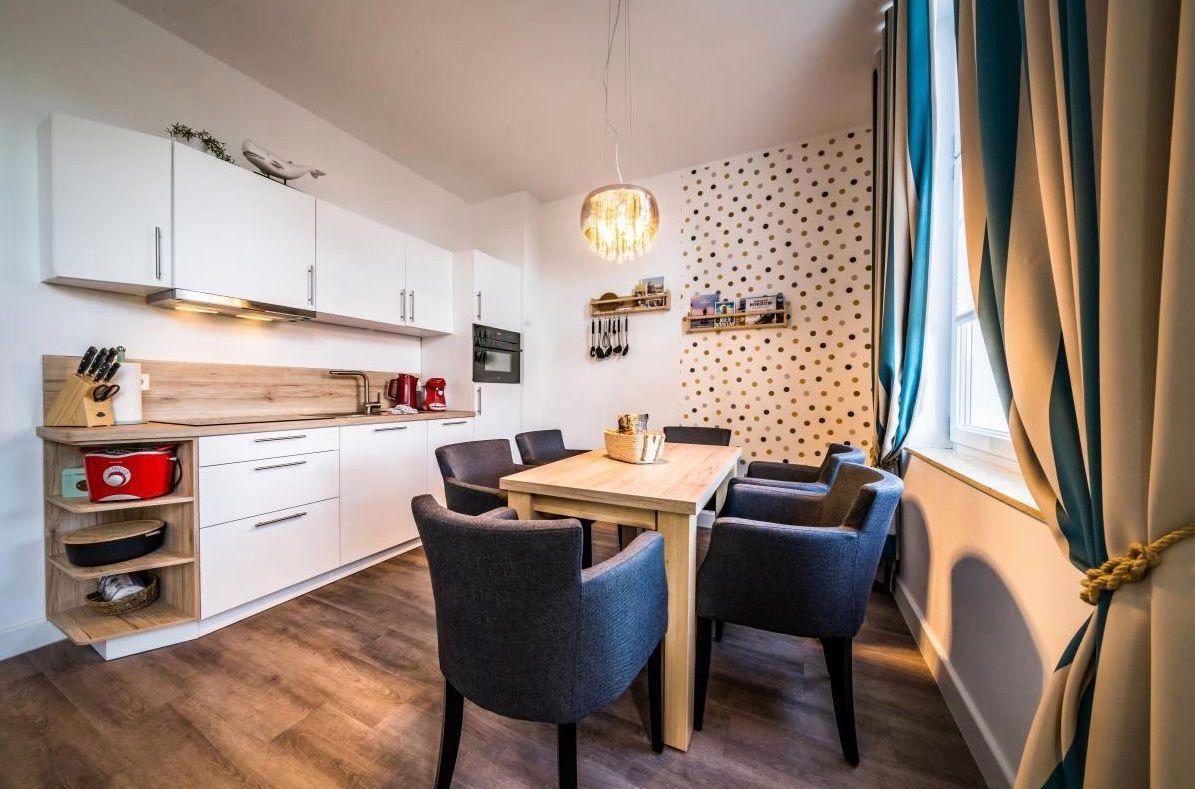 Küche mit Essbereich, Holztisch, grauen Stühlen und goldpunktiertem Wandpaneel.