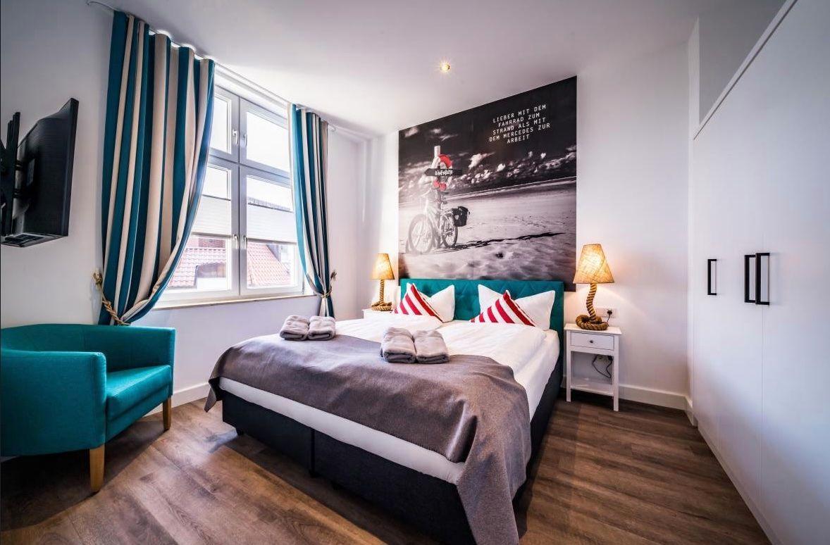 Schlafzimmer mit Bett, Fenster, TV und Wandbild.