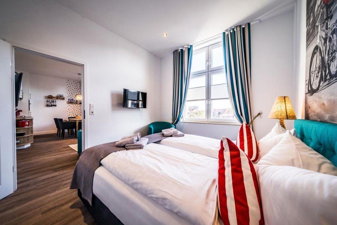 Zwei Betten mit weißen Bettwäsche, Fenster mit Streifen Vorhängen, Wandbild und Lampe.