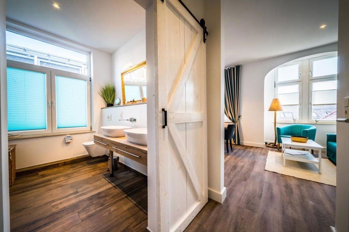 Badezimmer mit Doppelwaschbecken und Schlafzimmer mit grüner Couch.