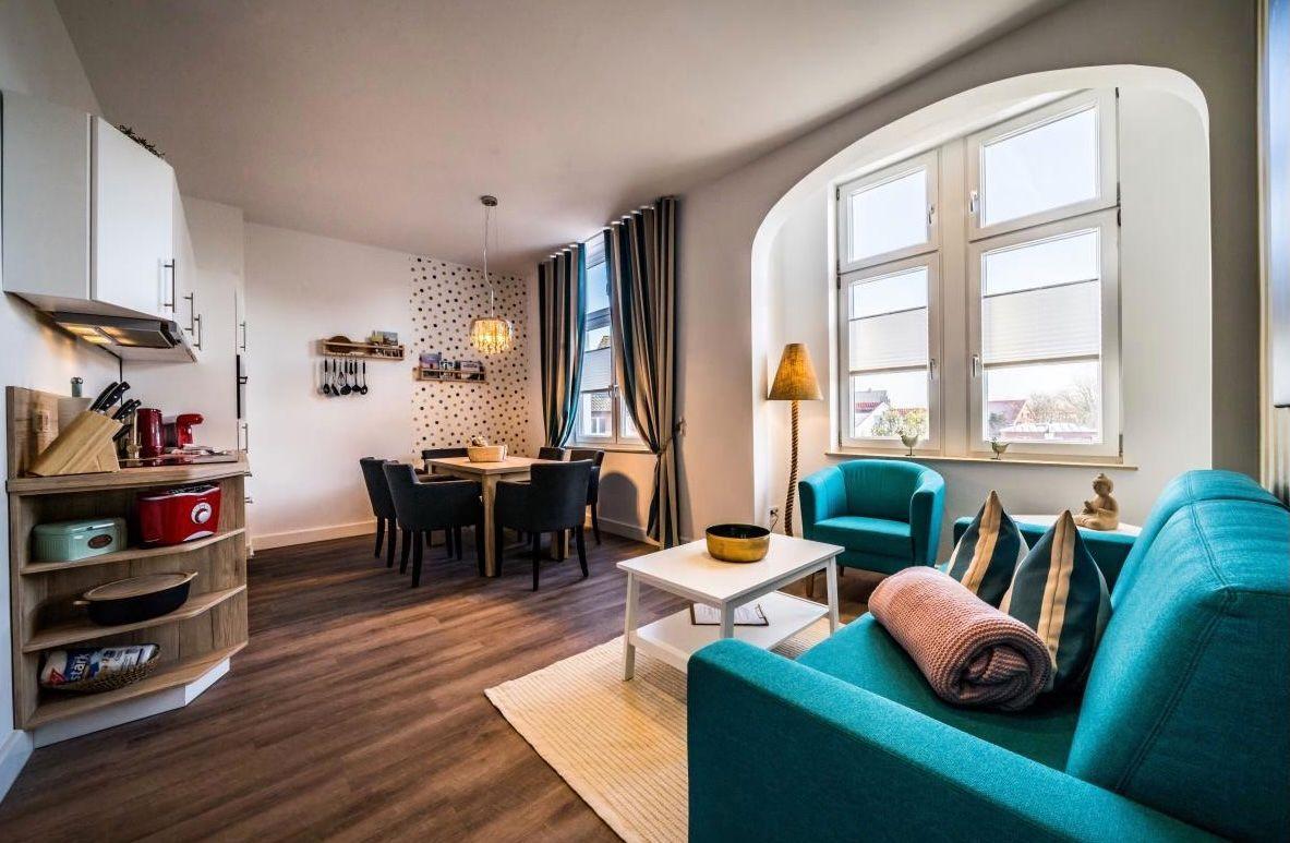 Wohn- und Essbereich mit Küchenzeile und großen Fenstern.