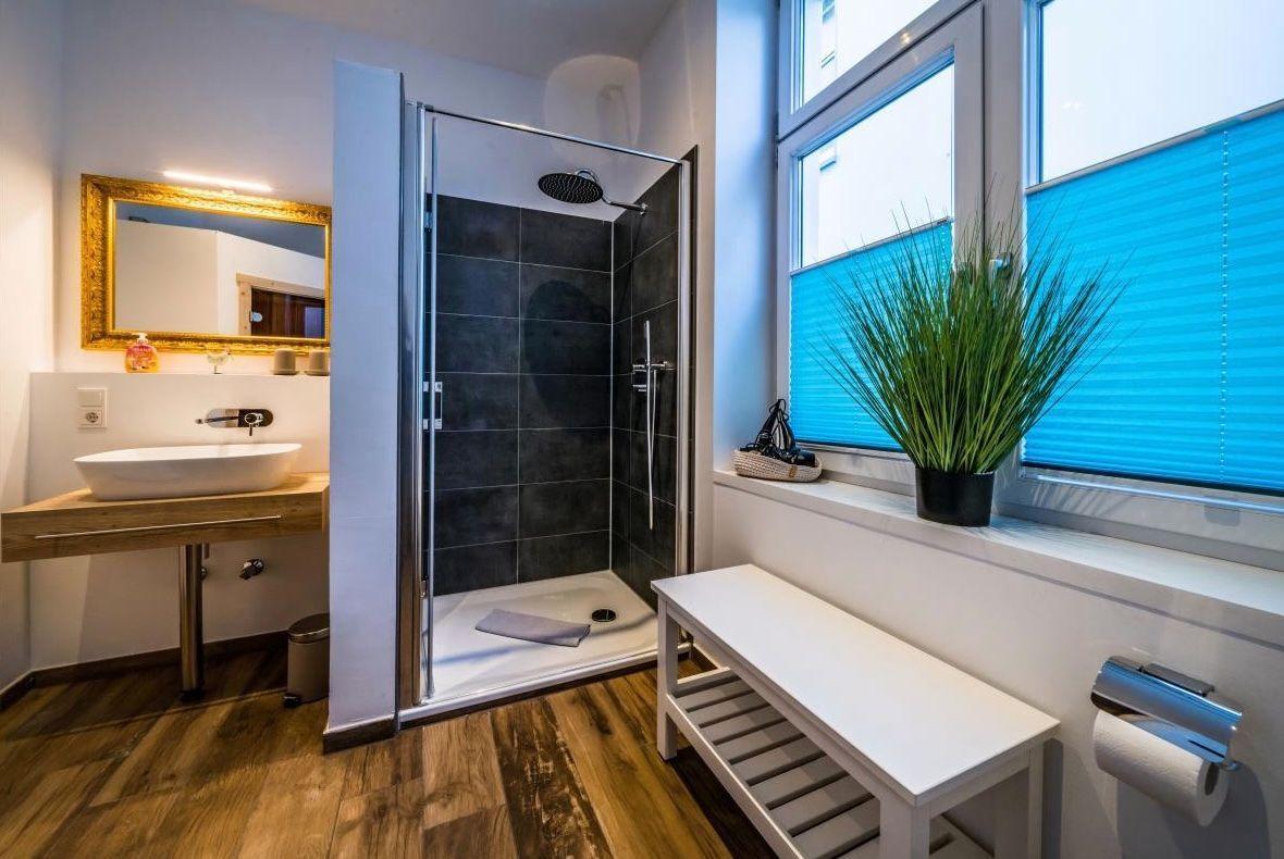 Badezimmer mit Dusche, Waschbecken und Fenster mit Pflanze.