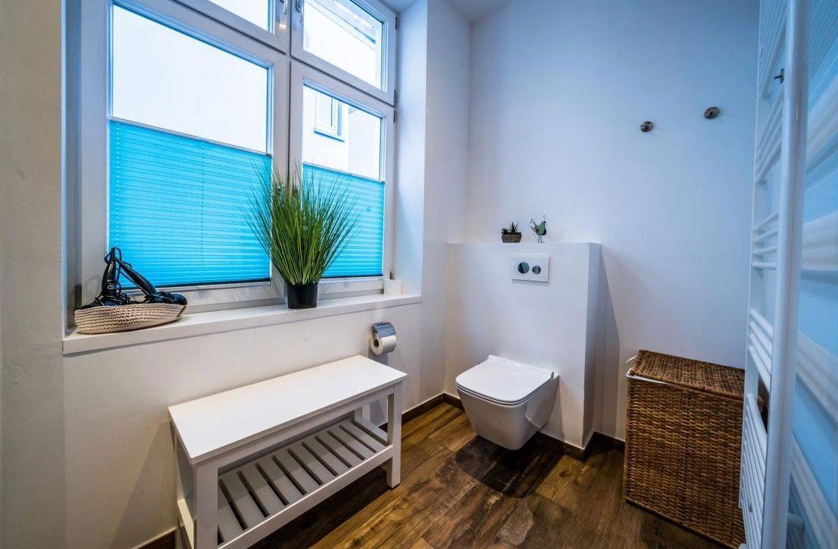 Badezimmer mit Toilette, Fenster, Bänkchen und Korb.