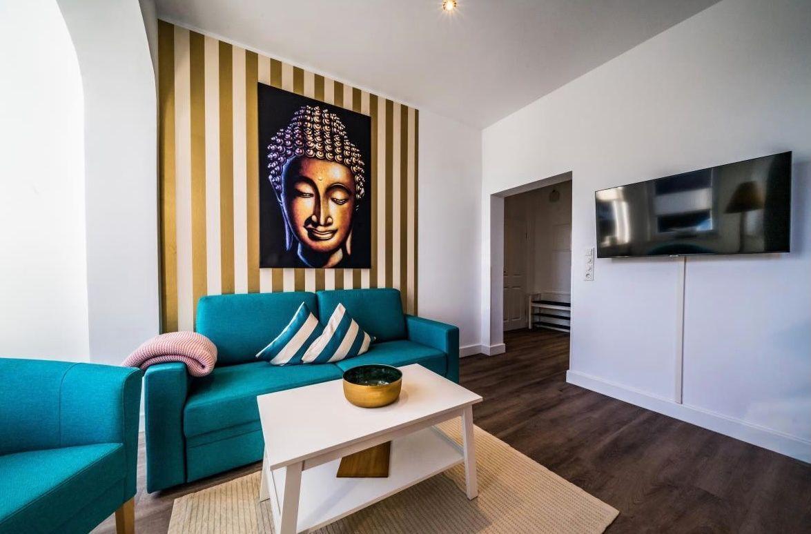 Wohnzimmer mit türkisfarbenem Sofa, Wandbild Buddha und Fernseher an der Wand.