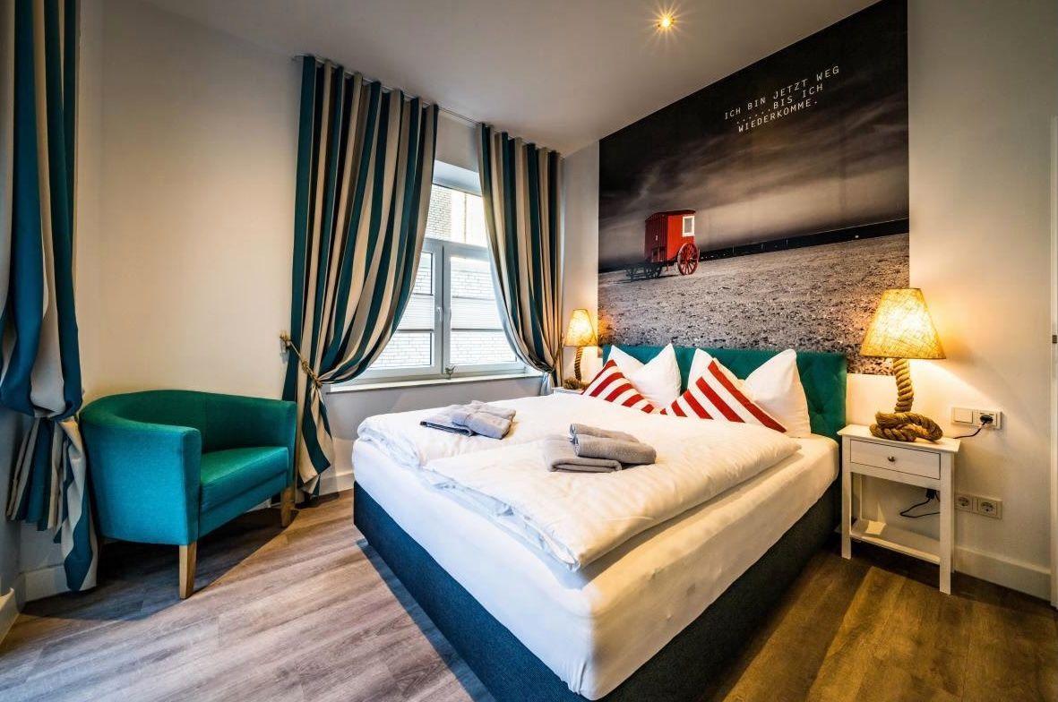 Schlafzimmer mit Bett, Sessel und Fenster mit Vorhängen.