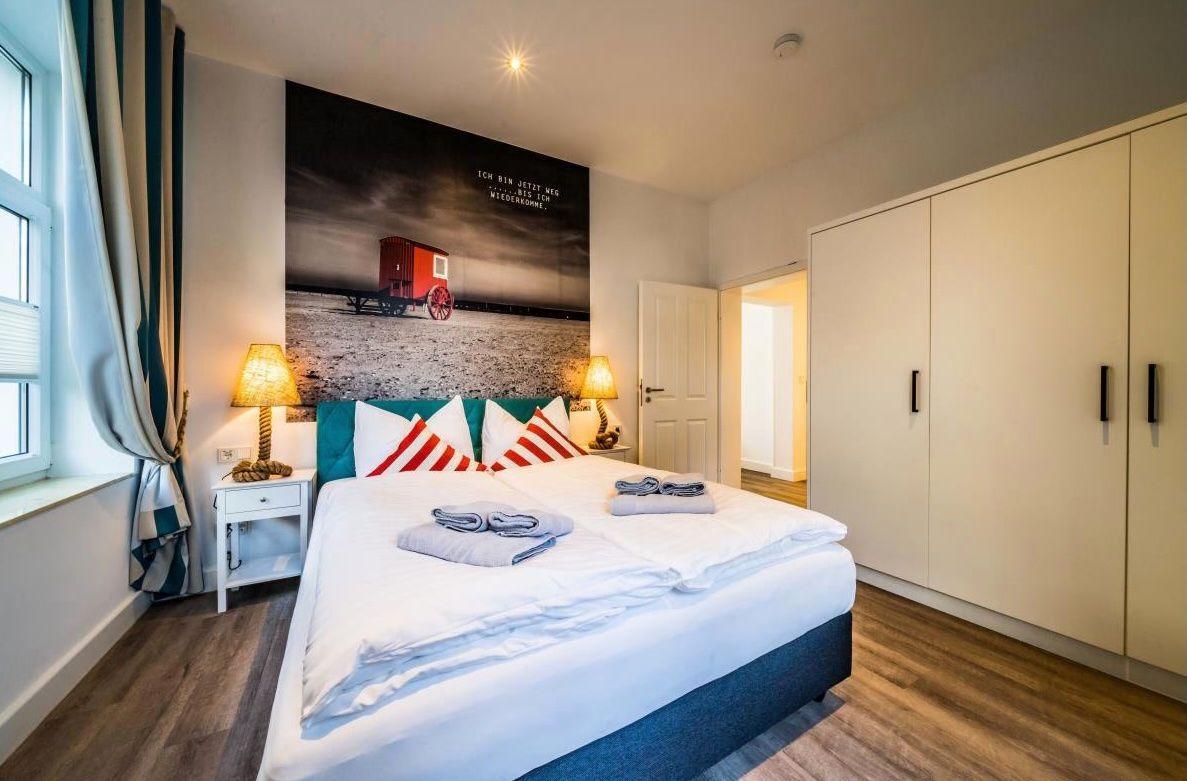 Schlafzimmer mit Bett, Kleiderschrank und Wandbild. Fenster mit Vorhängen.